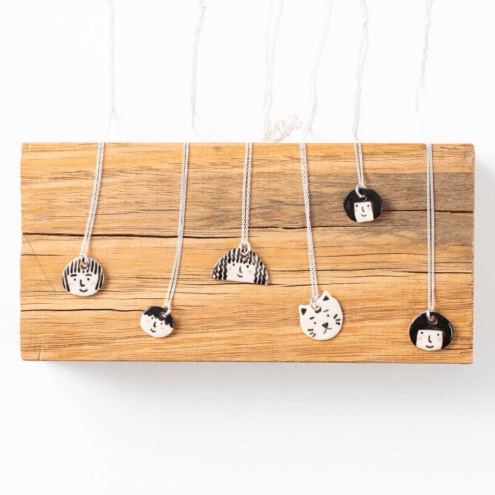 Collection of shuh. sterling silver necklaces, with handmade ceramic pendants and sterling silver chains, arranged on a wooden board. 