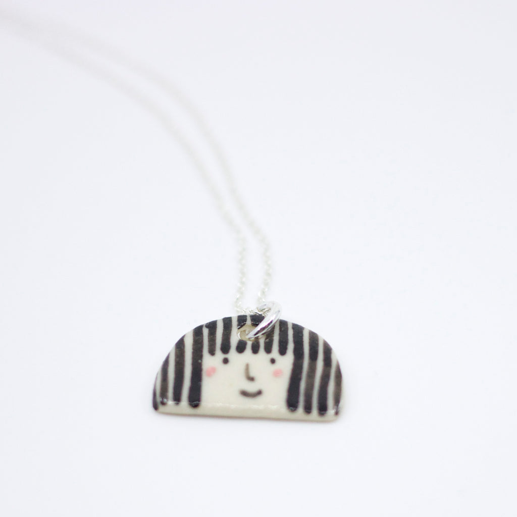Sterling silver necklace featuring a hand-painted ceramic pendant with a playful straight-haired face design, displayed on a white background.