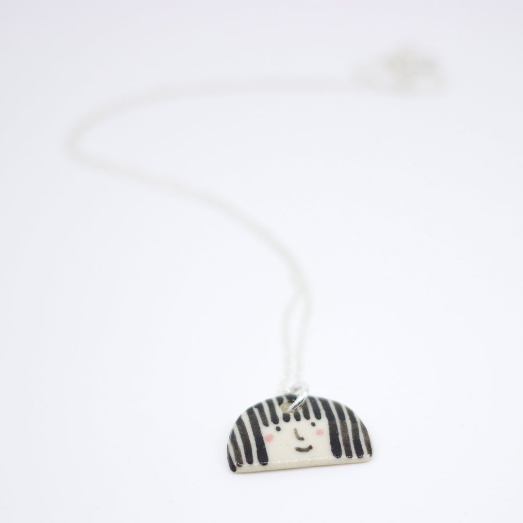 Sterling silver necklace featuring a hand-painted ceramic pendant with a playful straight-haired face design, displayed on a white background.