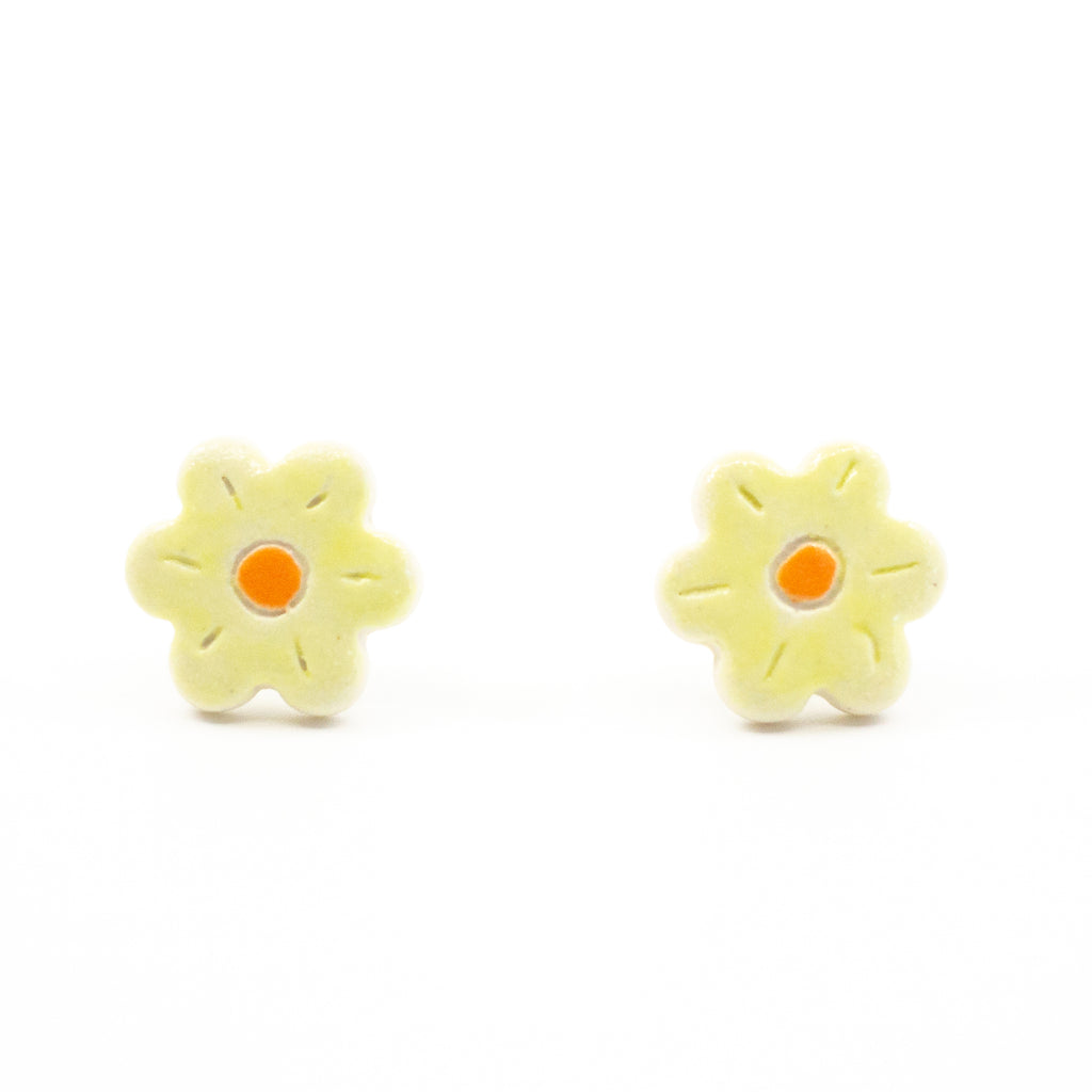 A pair of handmade ceramic stud earrings shaped like yellow flowers with an orange centre and carved petal lines. Finished with Sterling Silver posts.