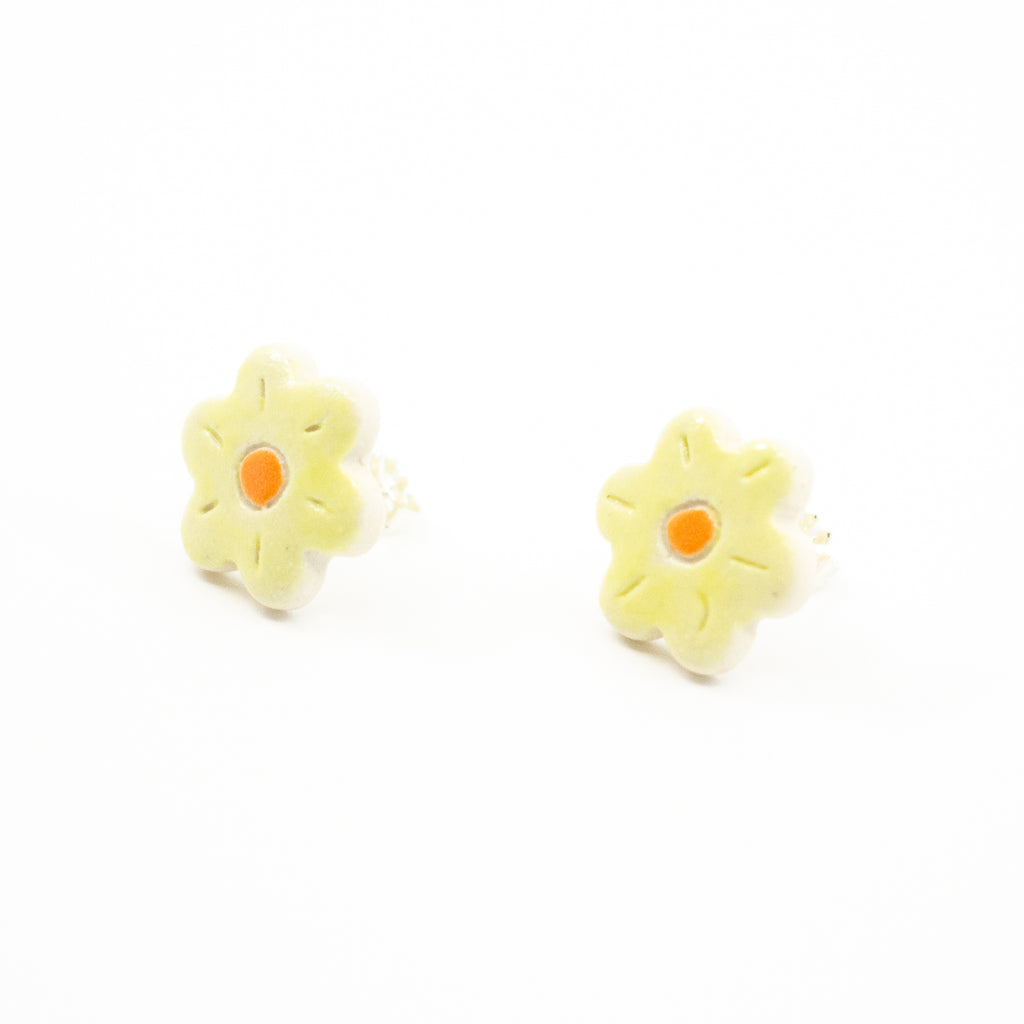 Side view of a pair of handmade ceramic stud earrings shaped like yellow flowers with an orange centre and carved petal lines. Finished with Sterling Silver posts.