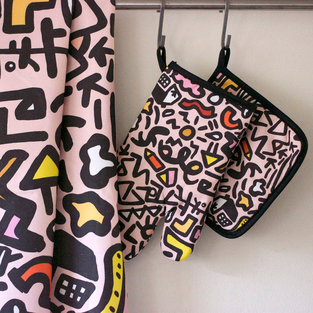 Front view of the sweet oven mitt, tea towel, and pot holder. Street inspired design, pink, black, and yellow designs on a pink background. 