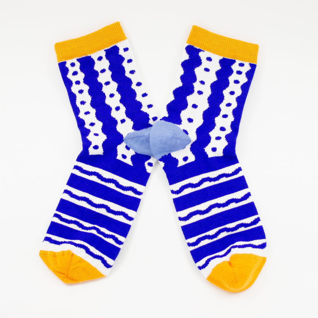 Front view of the TENGU socks. Featuring a bold blue and white pattern of playful waves, dots, and stripes, these socks bring energy and excitement to every step. The bright yellow cuff and toe add a pop of colour, while the soft blue heel keeps things stylish and unique.