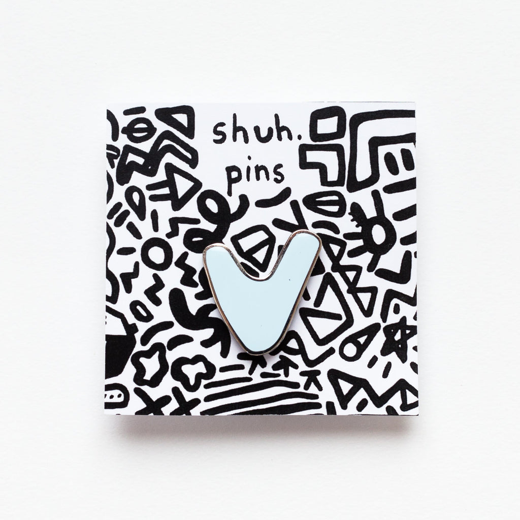 Small enamel pin with a stylised V shape, as though its arms are raised in celebration, displayed on white card with illustrated squiggles and “shuh. pins” branding.