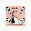 Enamel pin featuring a hand-drawn person and dog walking side-by-side in matching poses, displayed on a pink card with dog illustrations and “shuh. pins” branding.