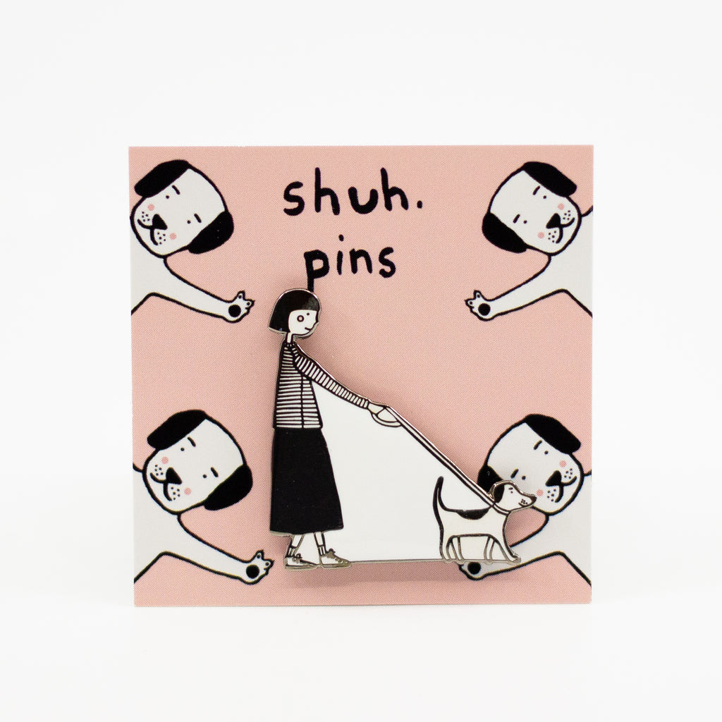 Enamel pin featuring a hand-drawn person and dog walking side-by-side in matching poses, displayed on a pink card with dog illustrations and “shuh. pins” branding.