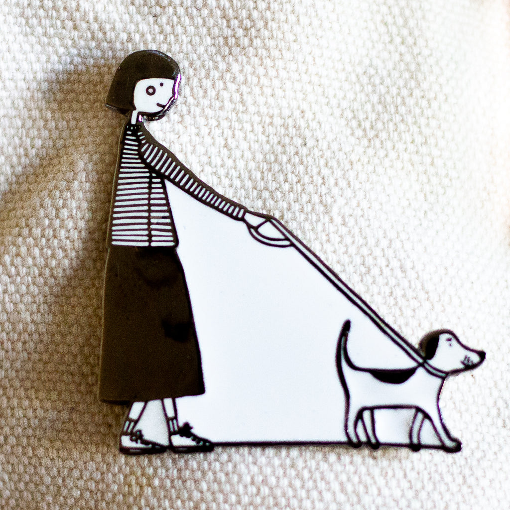 Enamel pin featuring a hand-drawn person and dog walking side-by-side in matching poses