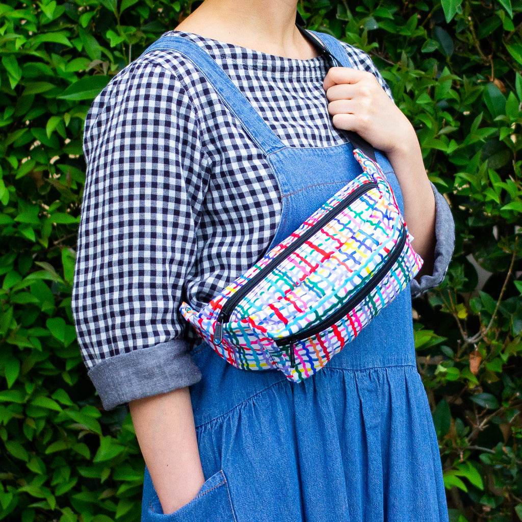The wave bumbag being carried across the shoulder. Pattern features wavy multicoloured lines on a black background. 
