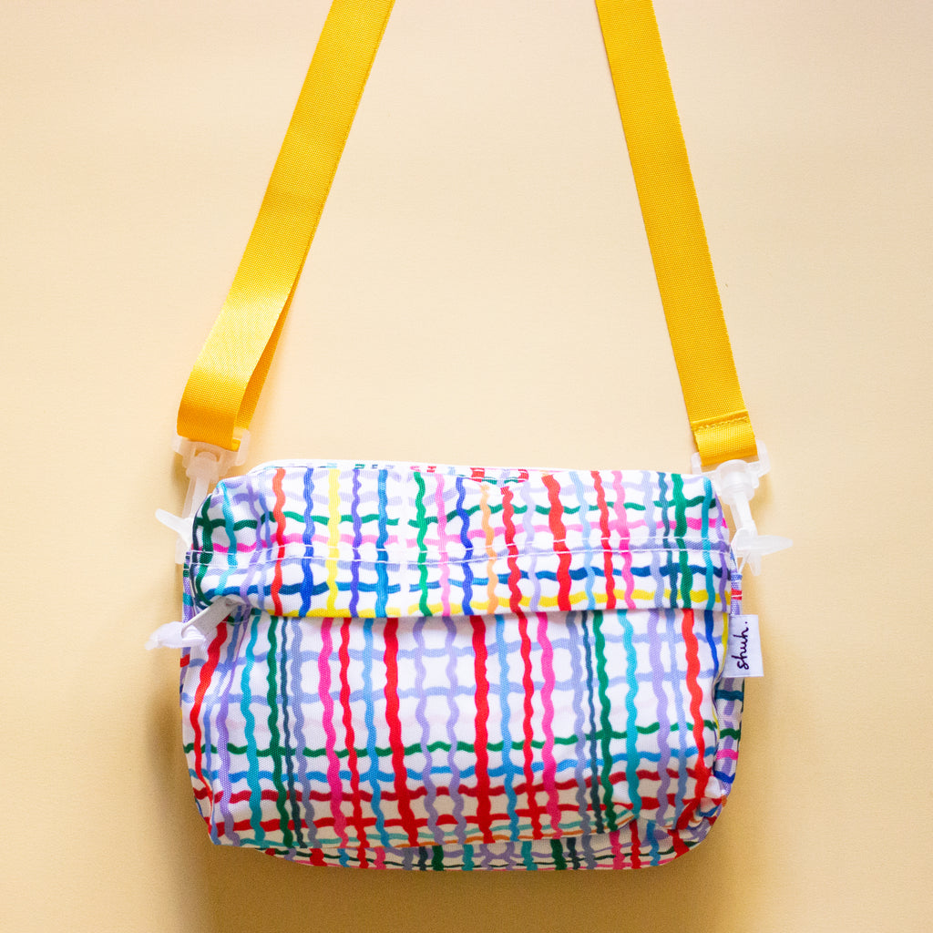 Front view of Wave everyday bag. With alternate Yellow strap. Multicoloured wavy lines on a white background.